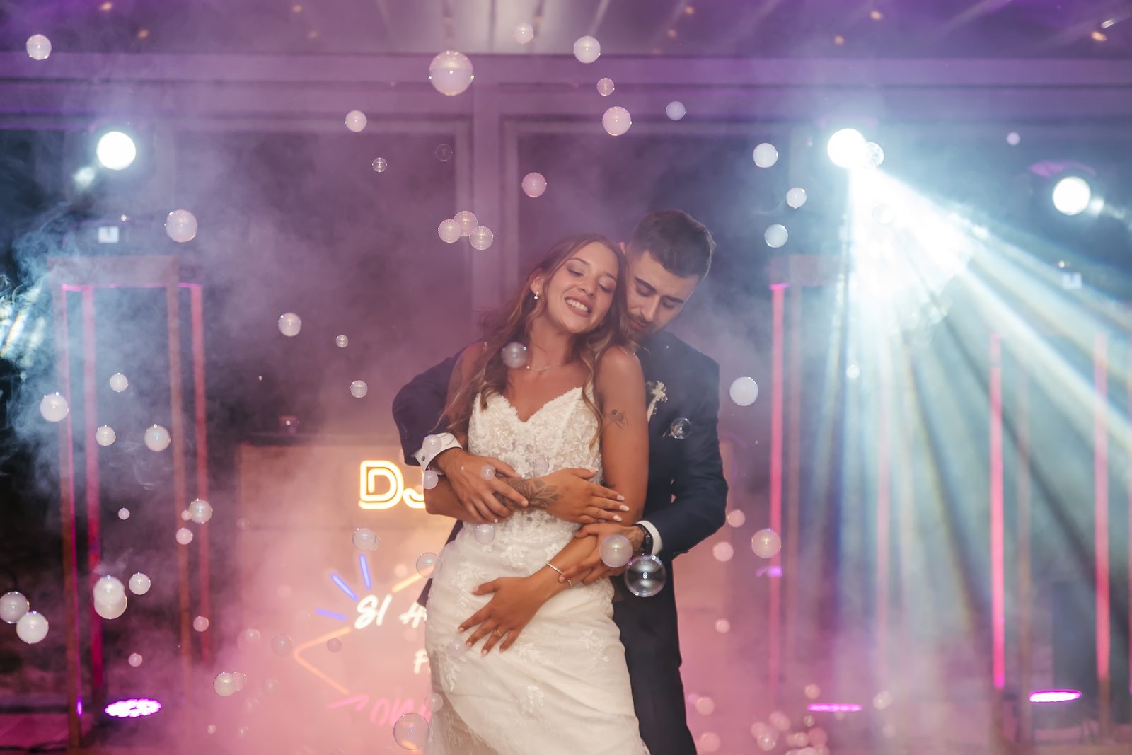Novios abrazados bailando entre burbujas y humo en la pista de baile